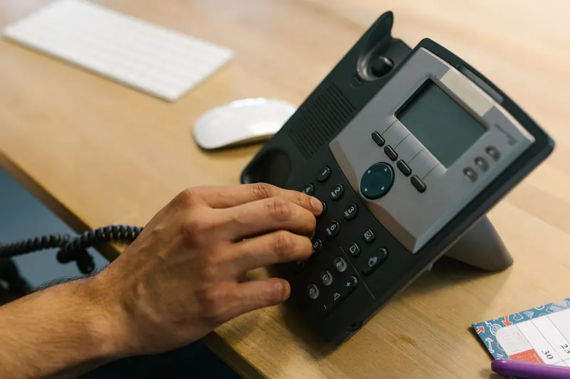 A hand dialling on the desk phone of an office